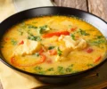 Moqueca de cação servida em uma panela de barro, com tomates, pimentões e coentro frescos.