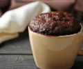 Bolo de chocolate na caneca pronto, fofinho e servido diretamente na caneca branca, com calda escorrendo por cima.