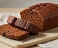 Pão de cacau caseiro dourado e fofinho, recém-saído do forno, servido em fatias sobre uma tábua rústica de madeira.
