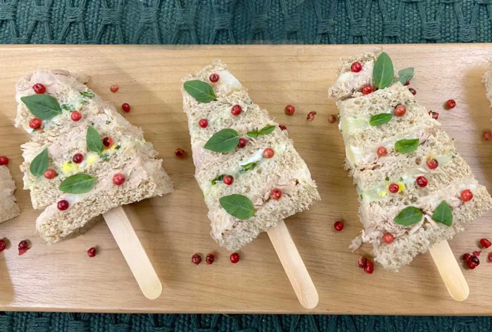 Sanduíches em formato de árvore de Natal decorados com pimenta rosa e manjericão.