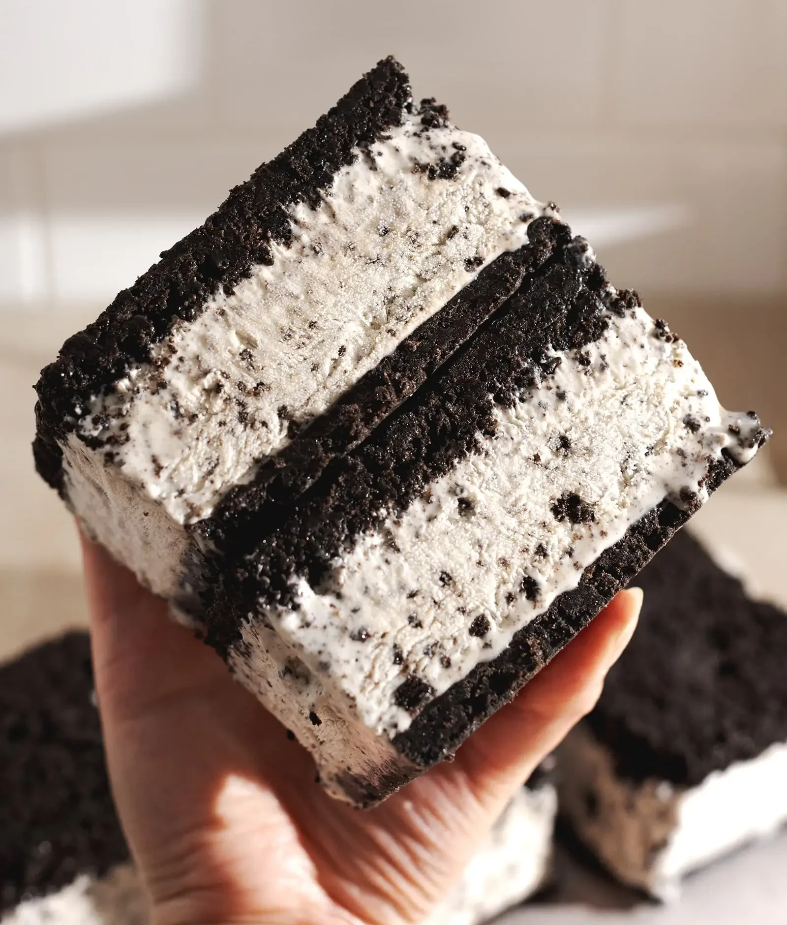 Mão segurando o sanduiche de sorvete feito de óreo.